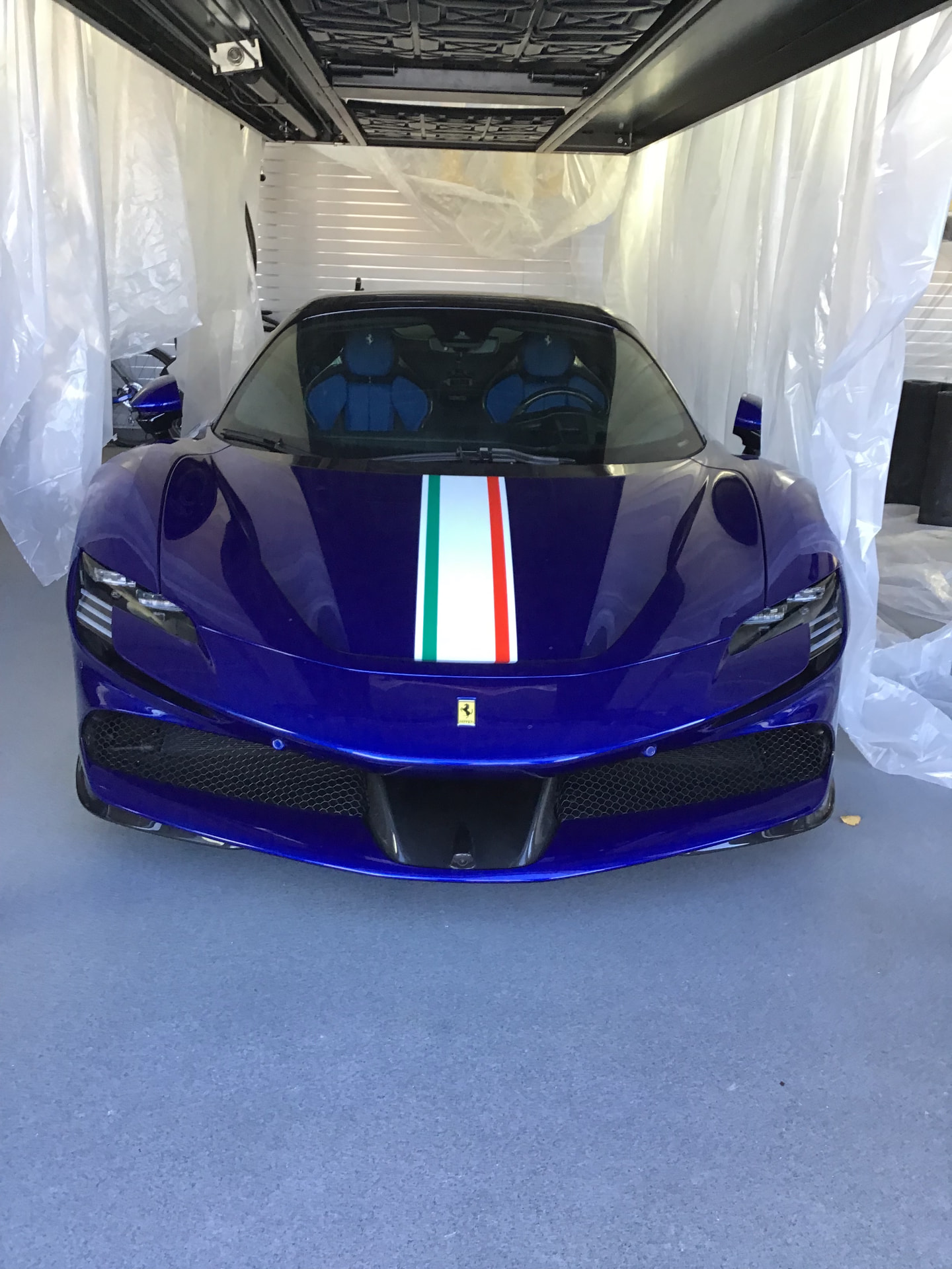 A blue Ferrari SF90 with Italian tricolore stripe in a climate-controlled garage